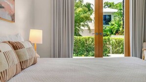 Quarto com cama, luminária e vista para um jardim através de uma porta de vidro.