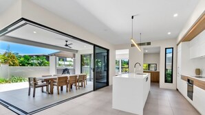Uma cozinha moderna com uma ilha central, uma sala de jantar com mesa e cadeiras, e vista para um espaço ao ar livre através de uma porta de vidro.