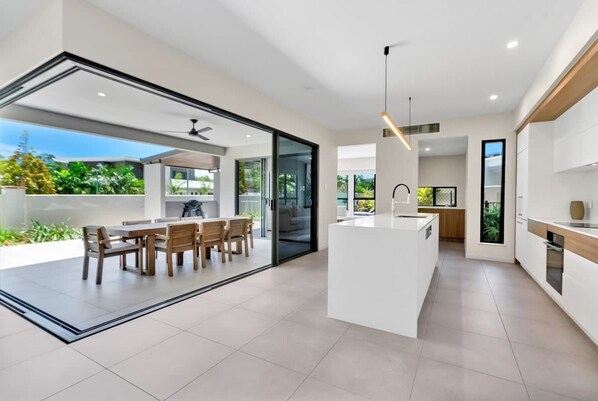 A modern kitchen with a central island, a dining area with a table and chairs, and a view through a glass door to an outdoor space.