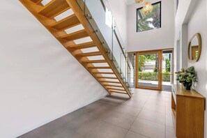 A modern interior with a wooden staircase, a glass door leading outside, and a wooden console table with a vase.