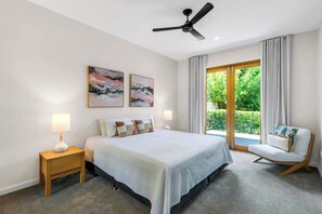 Une chambre à coucher comprenant un lit, des tables de chevet, un ventilateur de plafond, des œuvres d’art et une vue sur l’extérieur, visible à travers une porte vitrée.