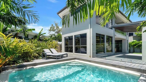 Uma casa moderna com piscina, espreguiçadeiras e vegetação exuberante.