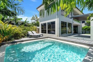 Une maison moderne dotée d’une piscine, de chaises longues et d’une végétation luxuriante.