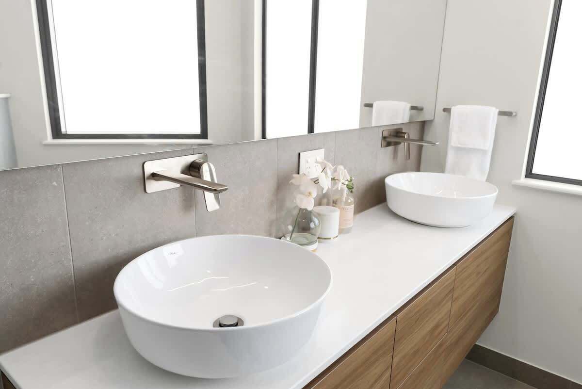 A modern bathroom with two white vessel sinks, a large mirror, and a window.