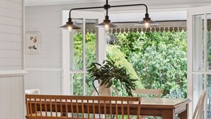 Een eethoek met een houten bank en tafel, twee hanglampen en een kamerplant.