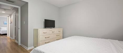 A bedroom with a bed, a dresser, a ceiling fan, and a television.