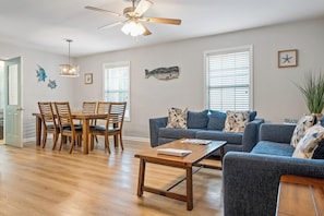 A living room with a dining area, wooden flooring, a ceiling fan, and wall decorations including fish and star motifs.