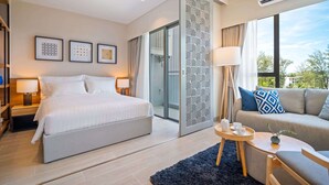 Une chambre d’hôtel moderne dotée d’un grand lit, d’un canapé, d’une petite table et d’une porte-fenêtre coulissante donnant sur un balcon.