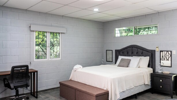 A bedroom with a bed, a desk, a chair, a bench, and a nightstand.