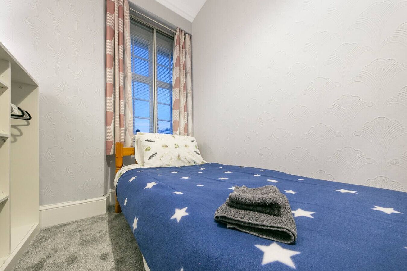 A bedroom with a bed, a window with curtains, and a patterned wall.
