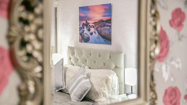 A bedroom with a tufted headboard, a bed with patterned bedding, and a painting above the bed. - Constancevilla B9 | Grampian Lettings Ltd (Bucksburn)