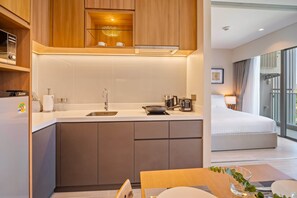 A modern hotel room with a kitchenette, a bed, and a large window.