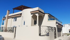 Una casa moderna de dos pisos con balcón, pérgola y una reja decorativa de metal.