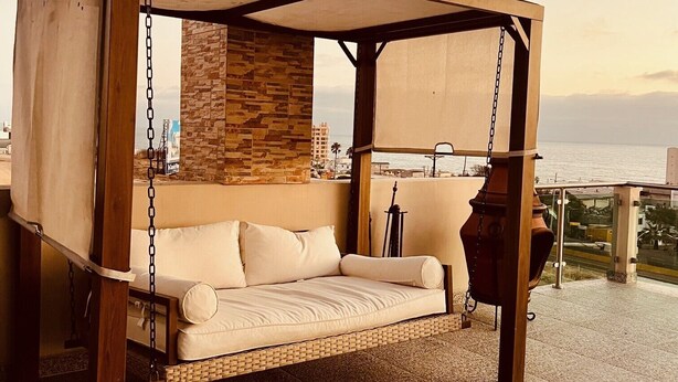 Una hamaca de madera con un muro de piedra de fondo, ubicada en una terraza con vistas al mar.