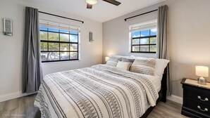 A bedroom with a bed, a ceiling fan, two windows with curtains, a nightstand, and a lamp. - Spacious 4BR Miami Townhome | Communal Pool (Miami)