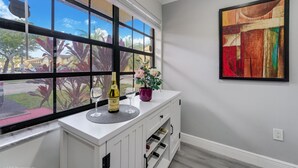 A room with a large window, a white cabinet with wine bottles, a glass of wine, and a potted plant. - Spacious 4BR Miami Townhome | Communal Pool (Miami)