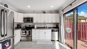 A modern kitchen with white cabinets, stainless steel appliances, and a large sliding glass door leading to a patio. - Spacious 4BR Miami Townhome | Communal Pool (Miami)