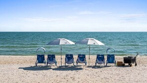 Ein Strand mit fünf blauen Liegestühlen und zwei Sonnenschirmen, einem Strandkorb und freiem Blick auf das Meer.