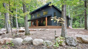 Une cabane en bois sombre, dotée d’un porche, entourée de gros rochers et d’arbres.
