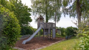 Un terrain de jeux avec un toboggan et des structures d’escalade, le tout entouré de verdure.