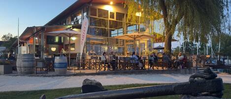 Un restaurante con terraza, fachada de vidrio amplia y un letrero que dice 'Staatsweinigt Meersburg'.