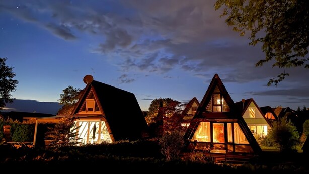 Une rangée de maisons de style traditionnel, avec des toits en pente, entourées d’arbres et dominant un paysage montagneux.