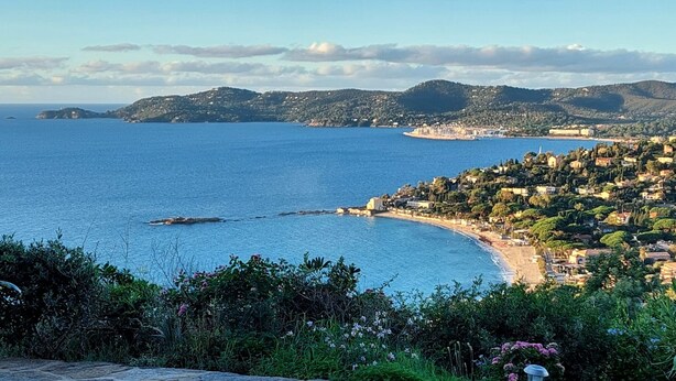A coastal town with a beach, hills in the background, and a clear sky.