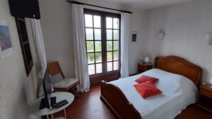A bedroom with a wooden bed, a chair, a small table, and a window with curtains.
