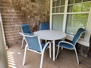 A patio with a round table and four chairs, a brick wall, and a window with blinds. - Rendezvous, a Resort Condo in charming Cape Charles. (Cape Charles)