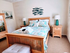 Een keurig opgemaakt bed met een bedspreide met patroon, twee nachtkastjes met lampen, een houten bankje en een decoratie aan de muur.