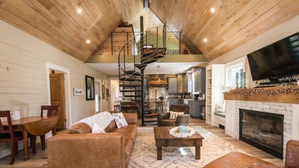 Un salon spacieux avec un canapé en cuir marron, une table basse et une cheminée. Un escalier mène à l’étage supérieur.