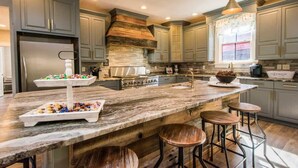 Une cuisine moderne avec des meubles gris, un grand îlot central doté de tabourets, une cuisinière encastrée et des luminaires suspendus.
