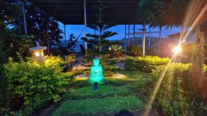 Un jardín sereno con una estatua de Buda, un farol y un área de descanso techada.