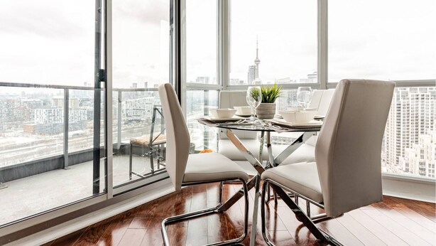 Un comedor moderno con una mesa de vidrio, sillas blancas y vistas a la ciudad.