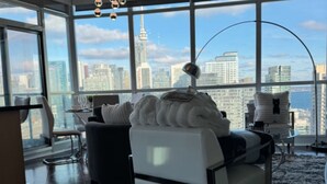 Habitación de hotel moderna con vistas a la ciudad, un ventanal grande, un sofá y un escritorio con lámpara.