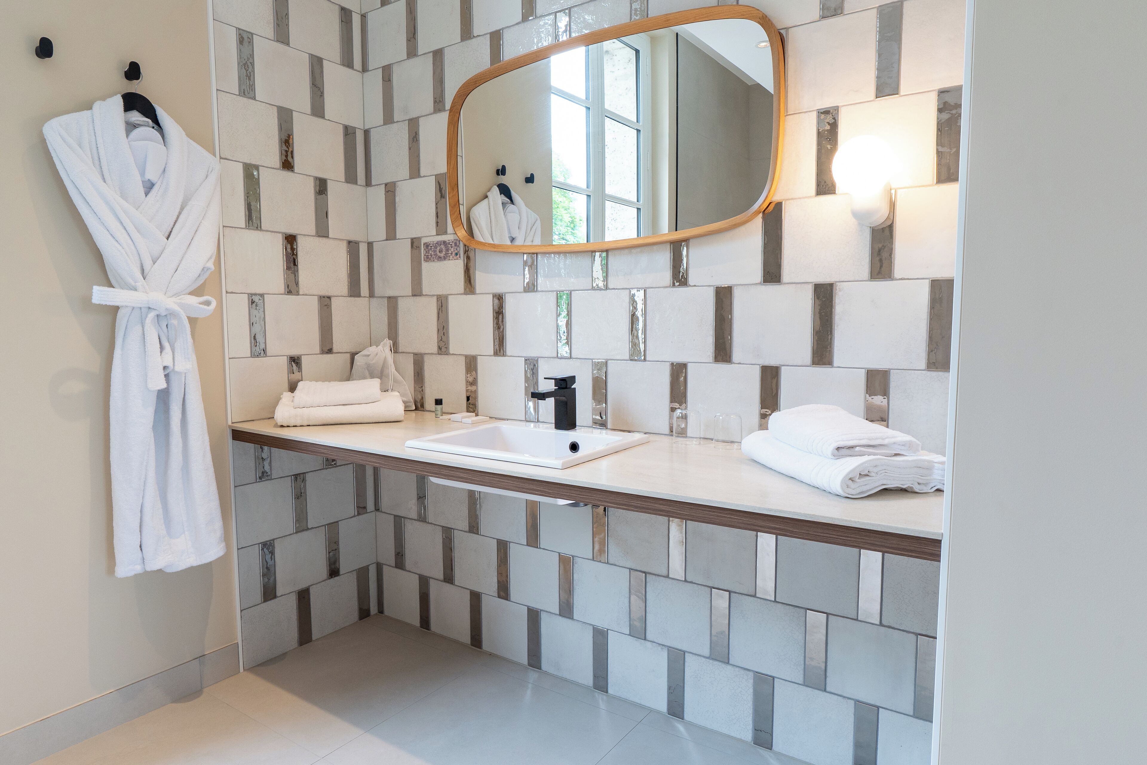 A bathroom with a tiled backsplash, a wooden countertop, a sink, a mirror, and a hanging bathrobe.