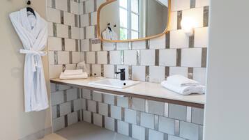 A bathroom with a tiled backsplash, a wooden countertop, a sink, a mirror, and a hanging bathrobe.