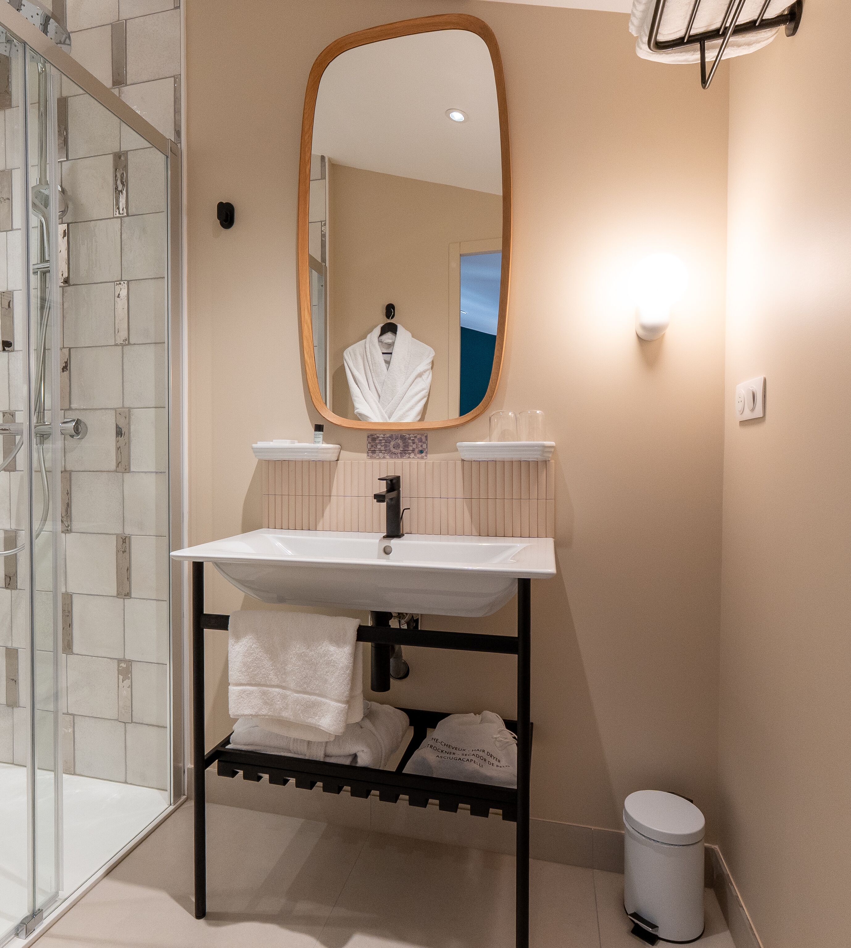 A bathroom with a white sink, a mirror, a towel rack, and a glass shower enclosure.