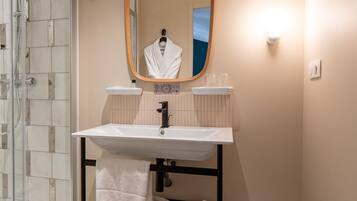 A bathroom with a white sink, a mirror, a towel rack, and a glass shower enclosure.
