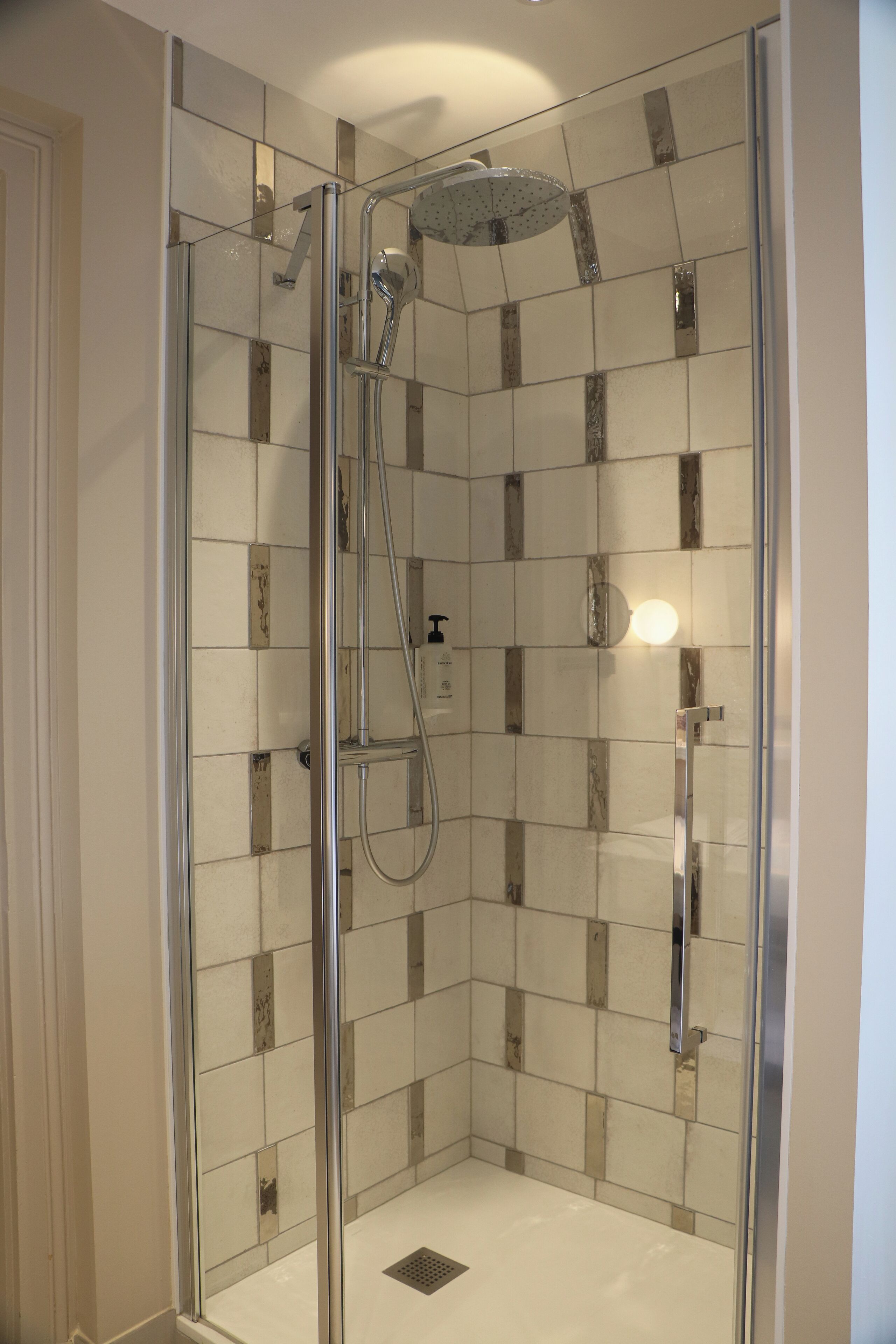 A glass-enclosed shower with a handheld showerhead and a wall-mounted faucet.