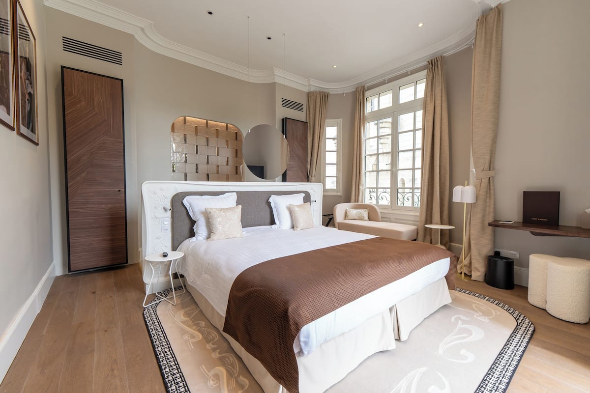 A modern hotel bedroom with a large bed, a bedside table, a chair, and a TV.
