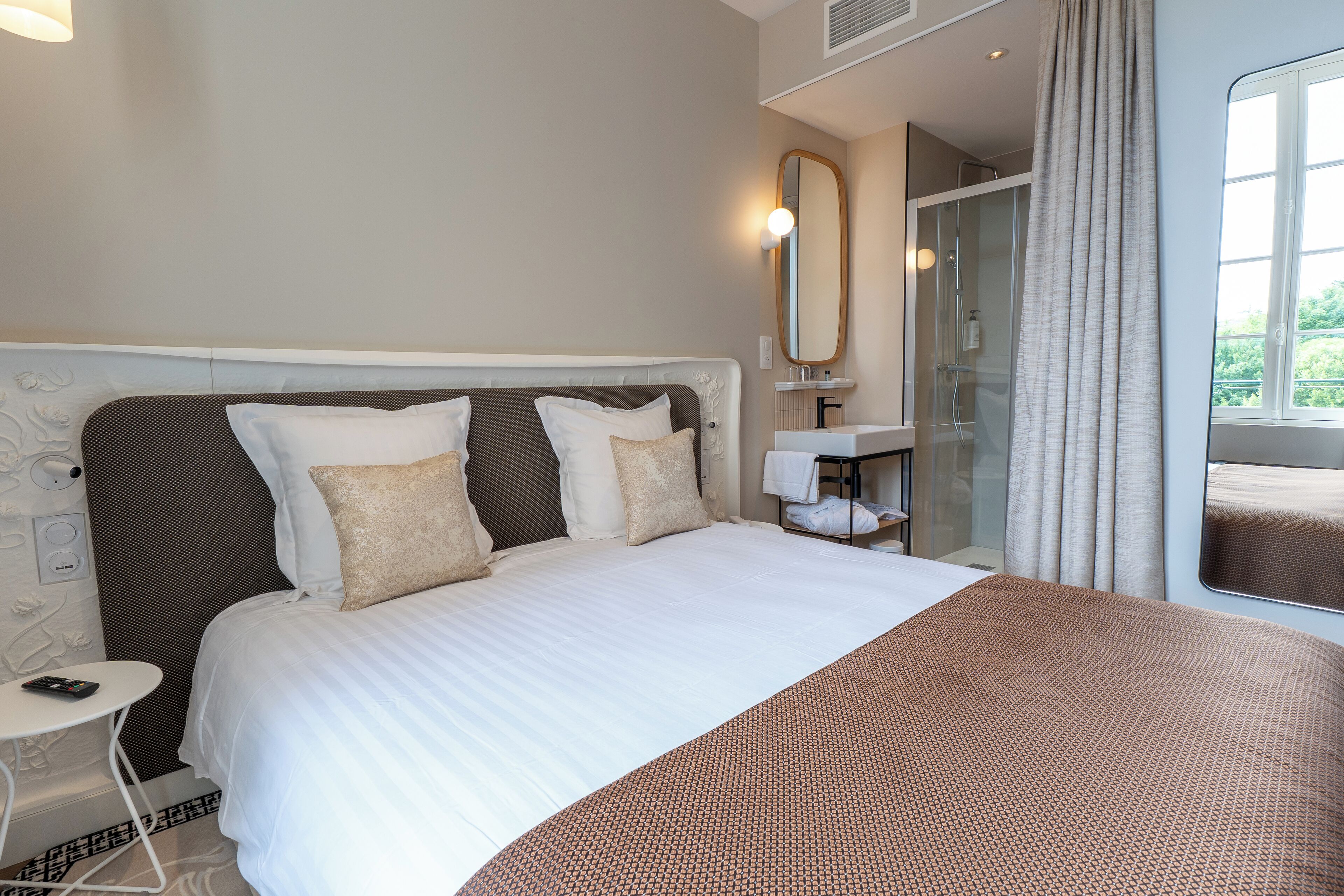 Une chambre d’hôtel avec un grand lit, une table de chevet, un miroir et une fenêtre avec des rideaux.