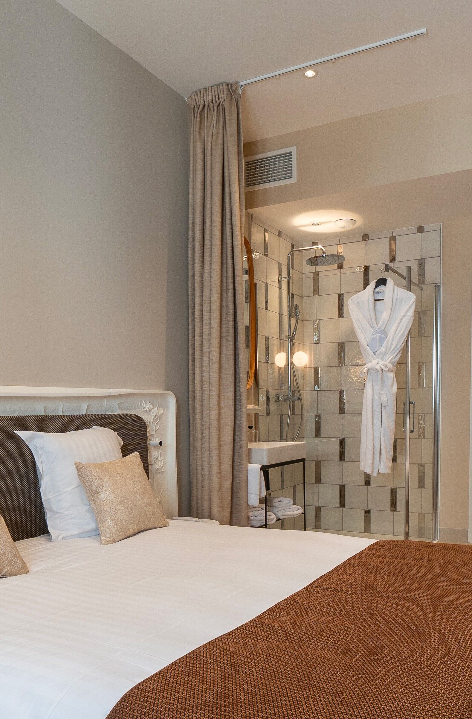 A hotel room with a large bed, a bathroom with a glass shower enclosure, and a robe hanging on the wall.
