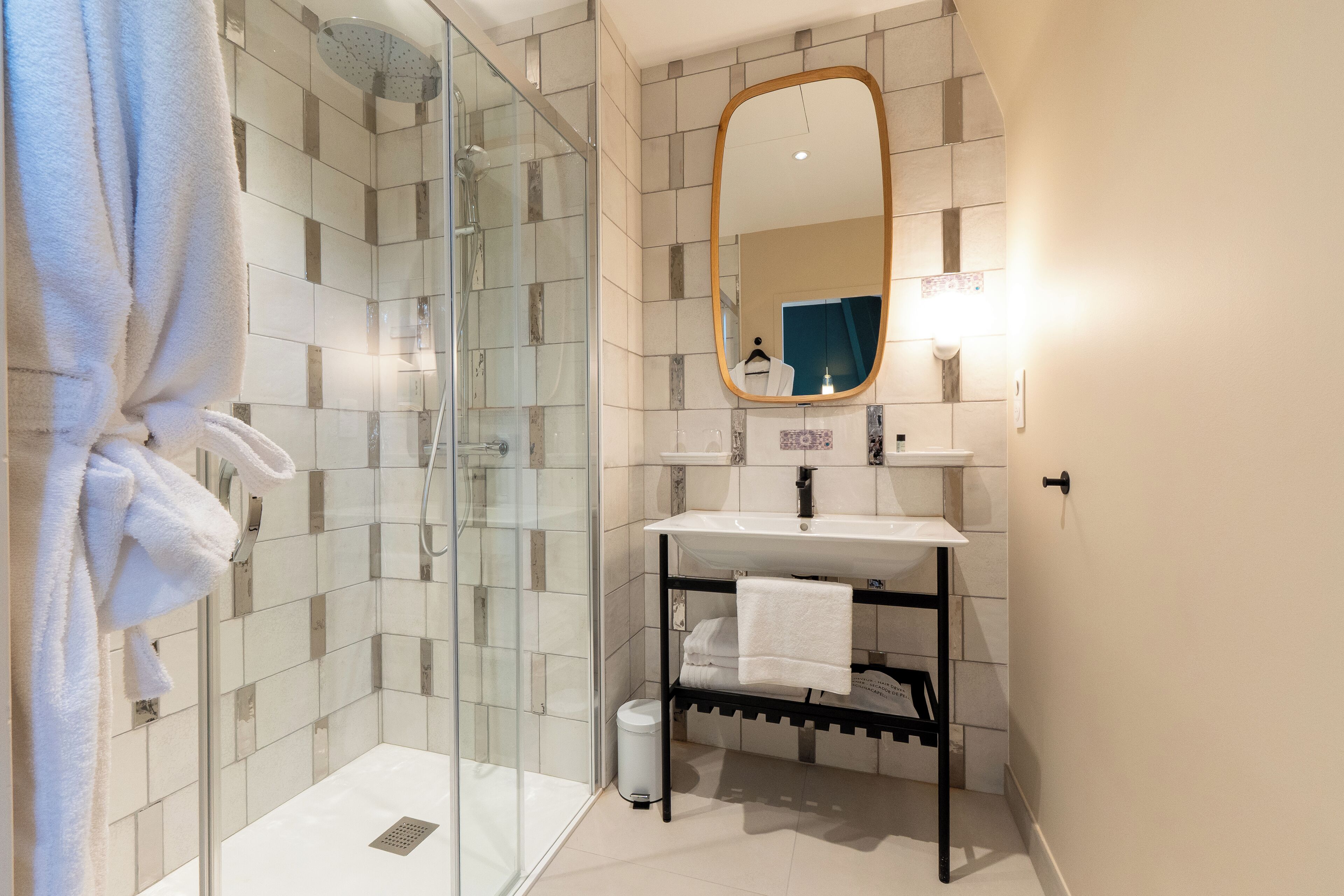 A modern bathroom with a glass-enclosed shower, a white sink, and a black towel rack.