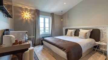 A hotel room with a large bed, a bedside table, a desk with a coffee maker, and a window with curtains.