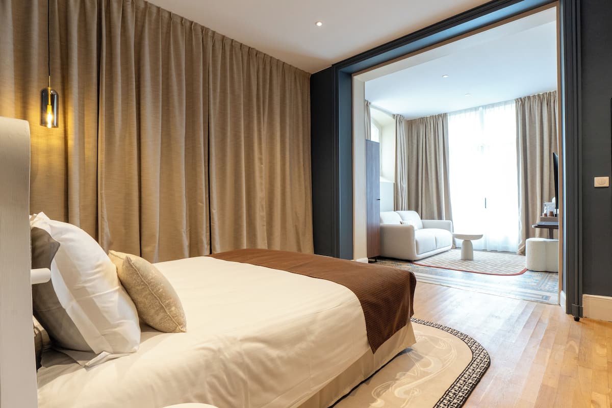 A modern hotel room with a large bed, a sitting area with a sofa and a coffee table, and a view of the balcony.