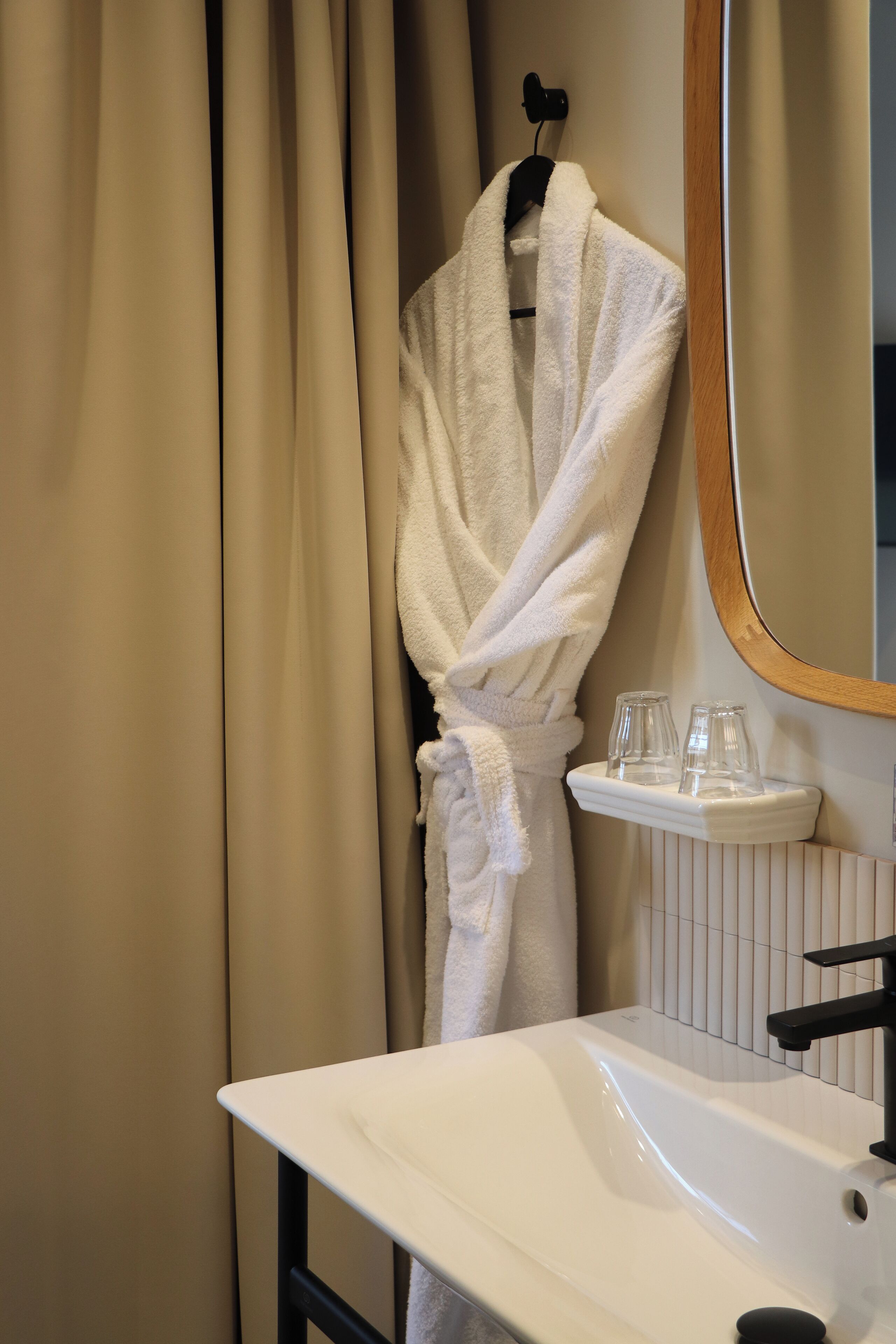 A bathroom with a white sink, a mirror, and a robe hanging on a hook.
