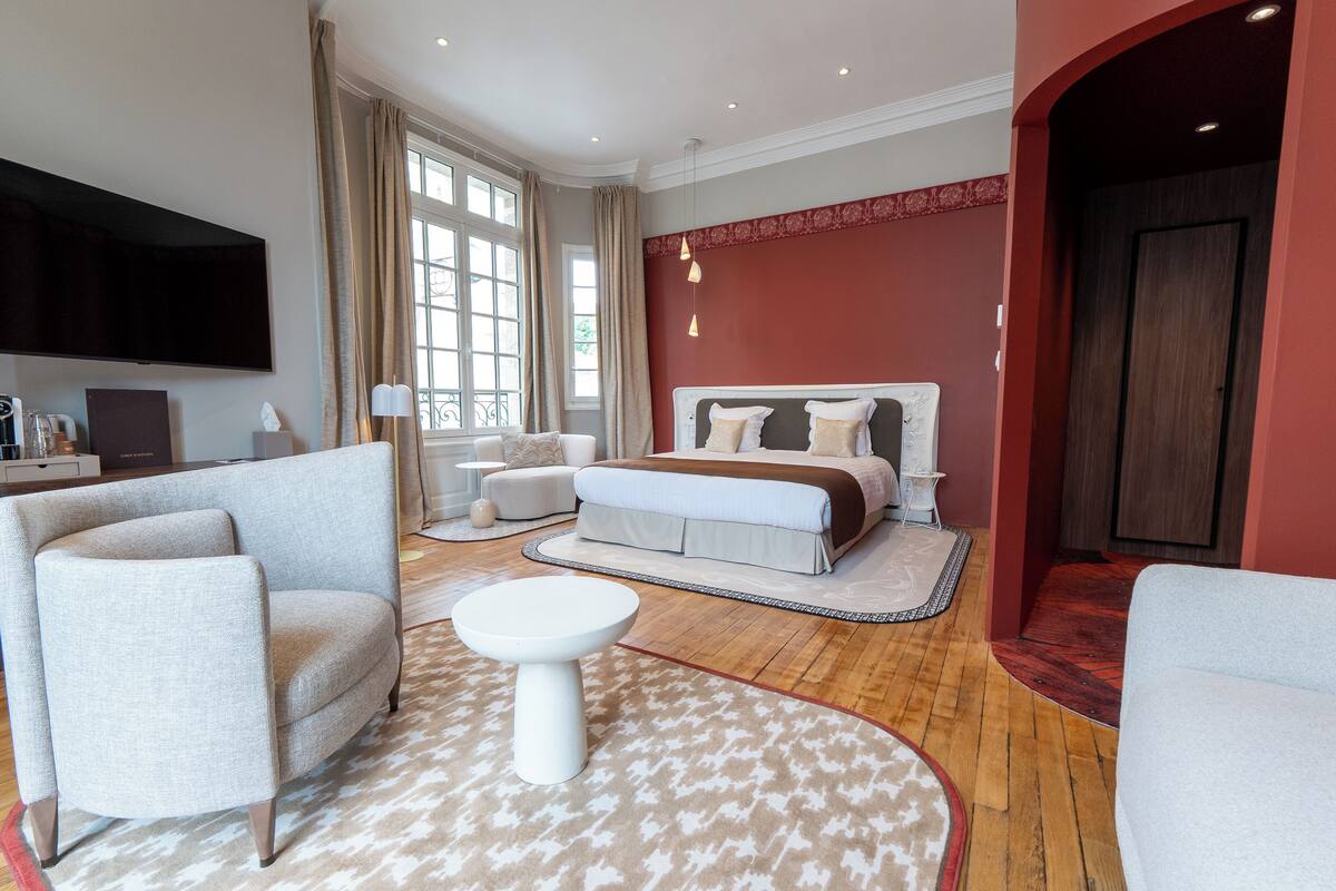 A modern hotel room with a large bed, a sofa, a small table, and a TV mounted on the wall.