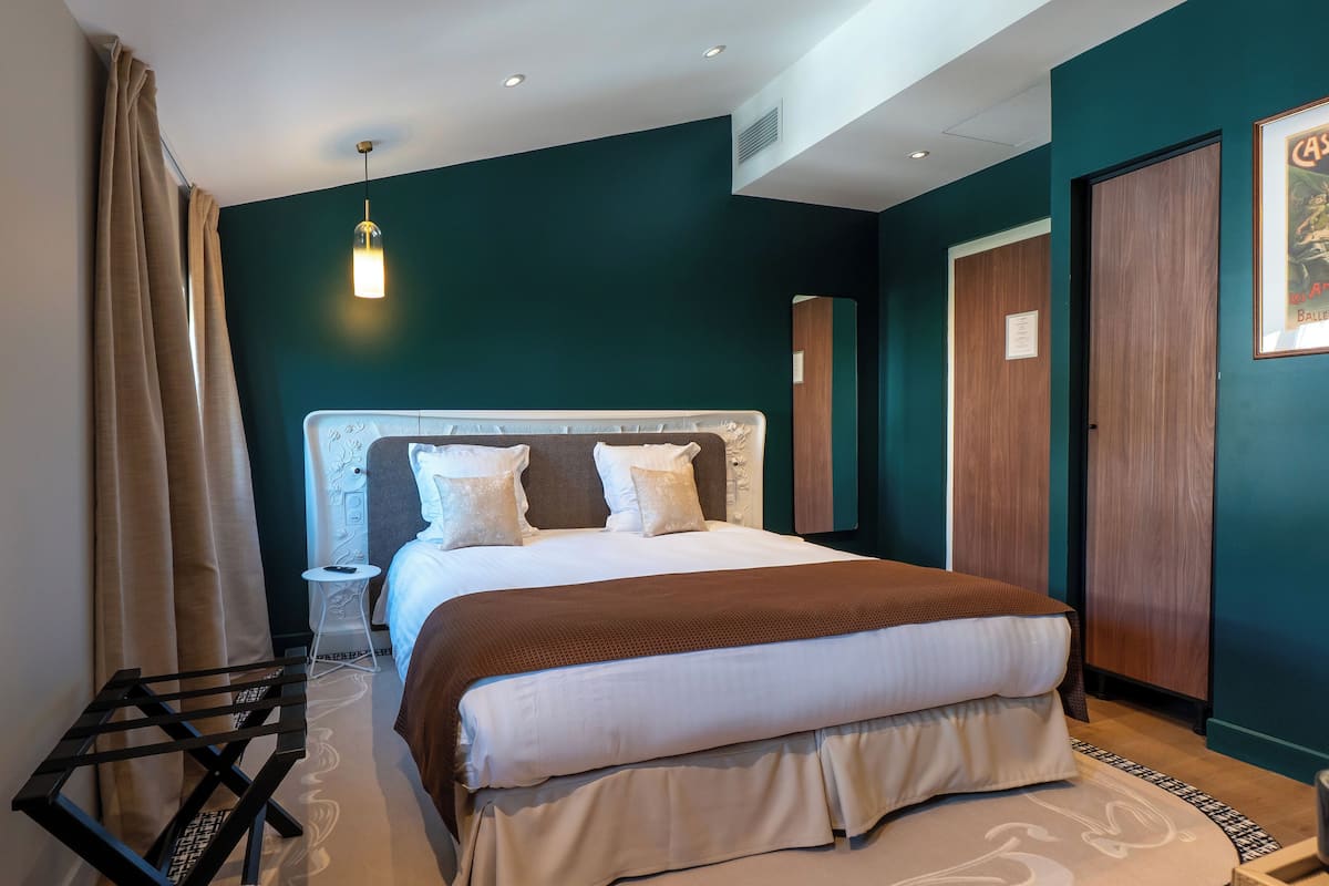 A modern hotel room with a large bed, a bedside table, a chair, and a hanging light fixture.