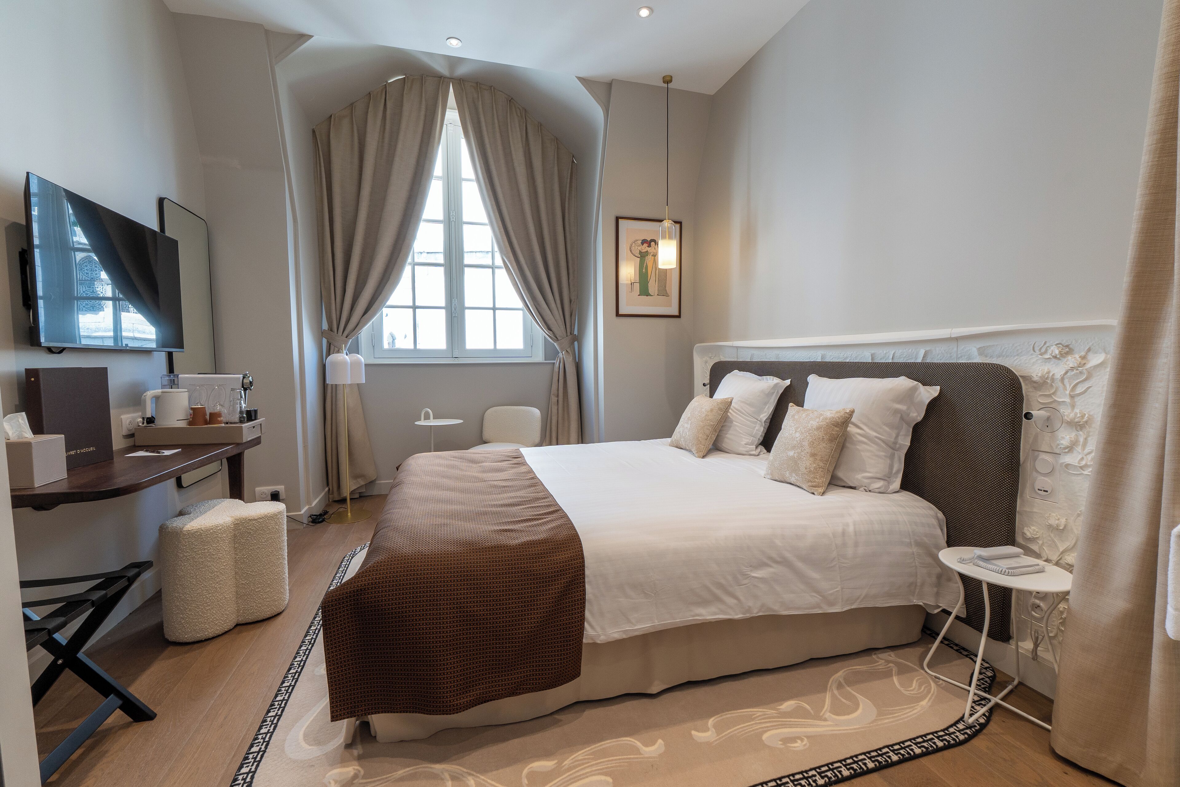 Un dormitorio de hotel moderno con una cama grande, un escritorio con silla, televisor y ventana con cortinas.